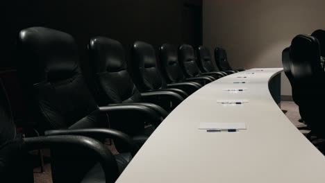 empty conference room featuring black chairs arranged around a long table with papers and pens laid out, ready for a meeting