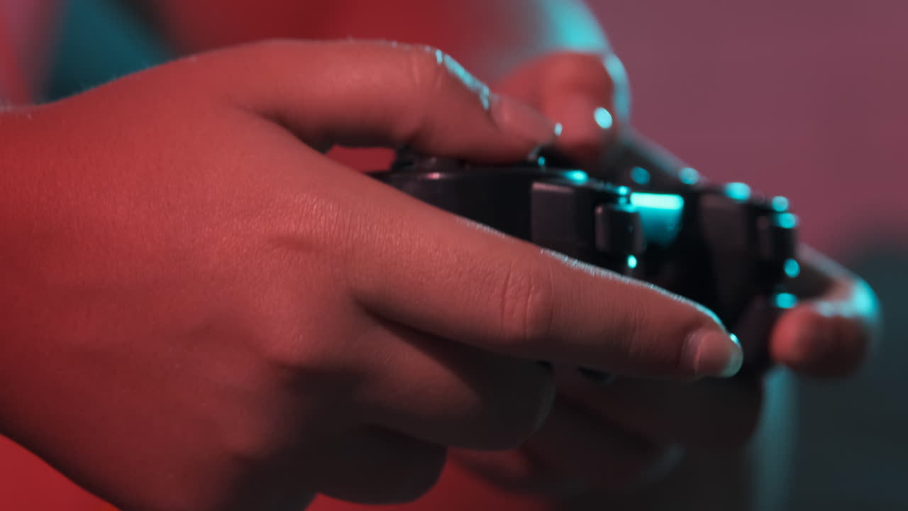 Close-up of women's hands with a game console controller while playing. Colorful lights
