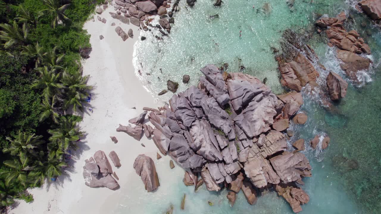 Pemandangan udara dari drone: batu granit dekat garis pantai, air pirus jernih, pantai berpasir putih, orang-orang snorkeling, pohon kelapa di dekat pantai, Anse Cocos, La Digue, Seychelles 008.