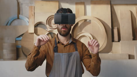 caucasian young bearded man in apron and vr headset, scrolling and tapping with hands in air in workshop