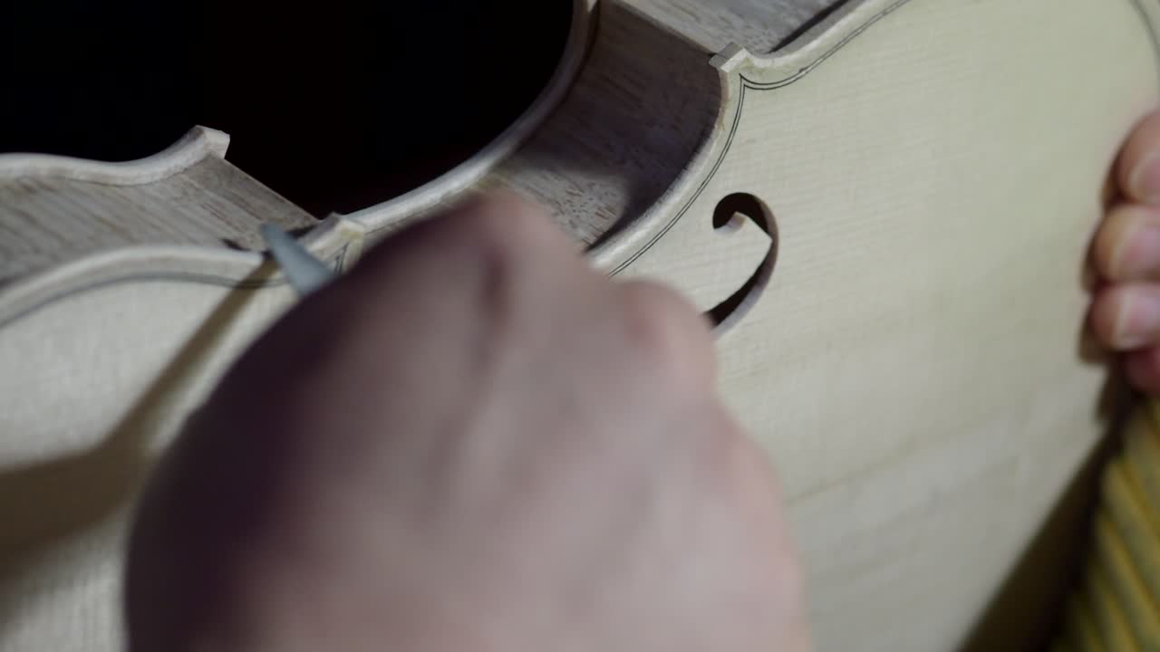Close-up of luthier carving spruce violin top plate edge around the f-hole and purfling area, demonstrating precise craftsmanship, traditional methods, and attention to acoustic and aesthetic detail