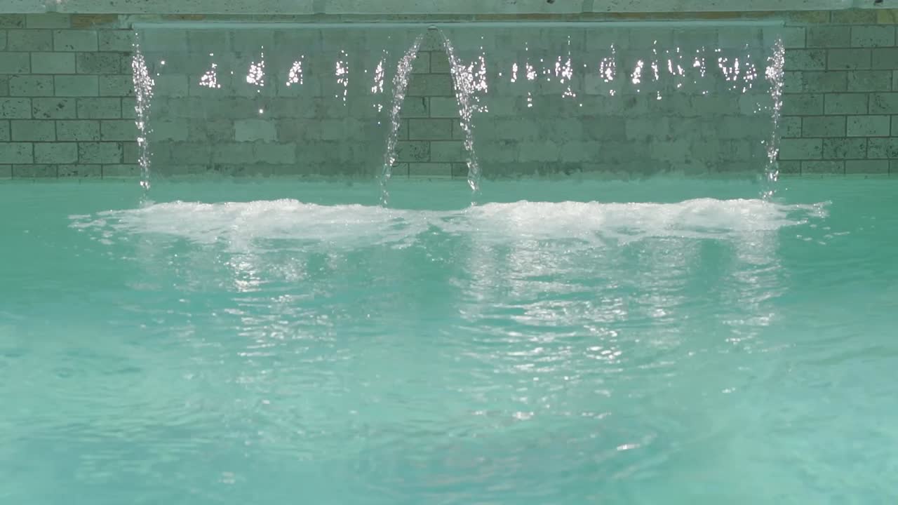 Frontal udsigt til udendørs swimmingpool med vandfald i et luksuriøst resort-spa.