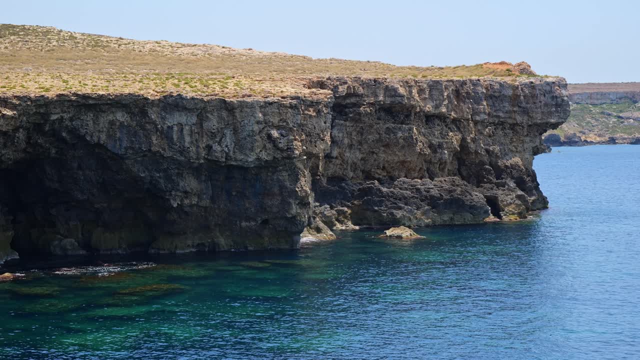 Stunning coastal view of tall cliffs by calm blue water on a bright, hot summer day. Peaceful nature scene