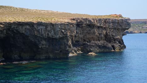stunning coastal view of tall cliffs by calm blue water on a bright, hot summer day. peaceful nature scene