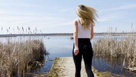 fun confident young woman runs out on to a dock on a beautiful calm lake