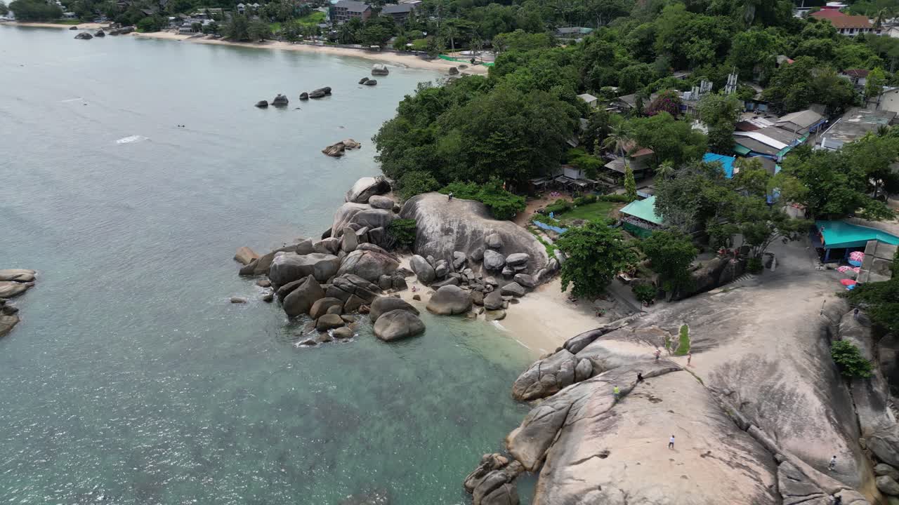Panoramic aerial shot of a Rocky beach with lush green mountains adjutant to it