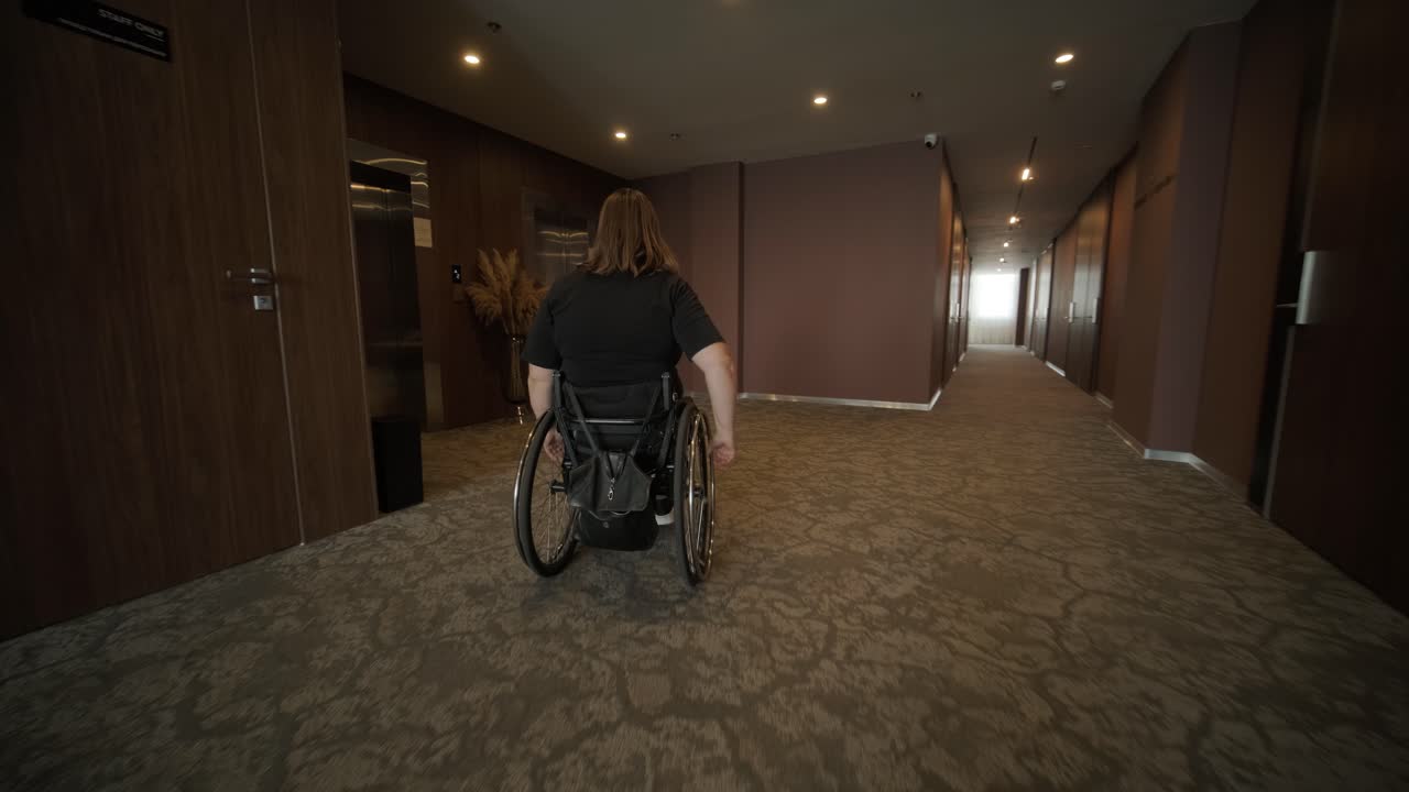 una mujer en silla de ruedas se acerca a un ascensor en el vestíbulo de un hotel, mostrando alojamientos accesibles y diseño moderno. la escena hace hincapié en la movilidad, la independencia y la inclusión en la hospitalidad.