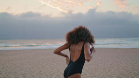 Excited-girl-running-seashore-raising-hands-up-overcast-evening.-Woman-have-fun.