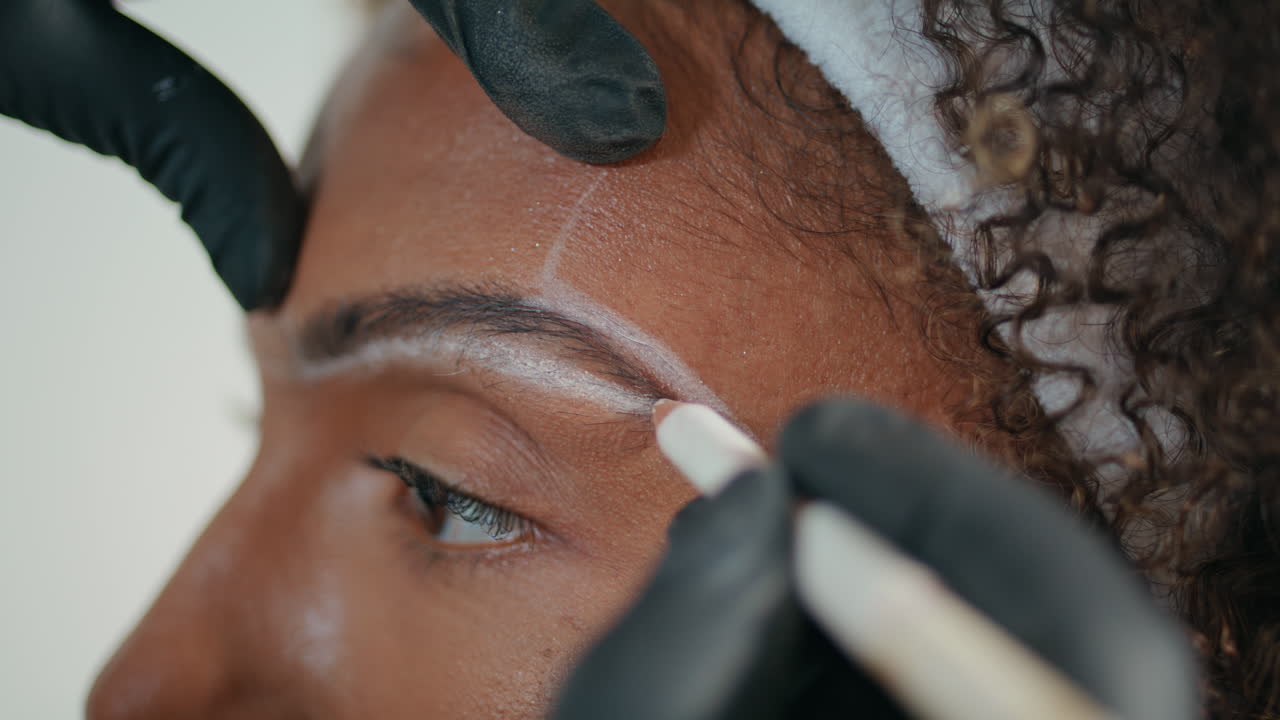 cosmetician de primer plano marcando las cejas con lápiz. manos en guantes formando el contorno
