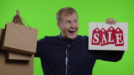 surprised guy showing shopping bags and sale word, looking astonished by low cost purchase, discount