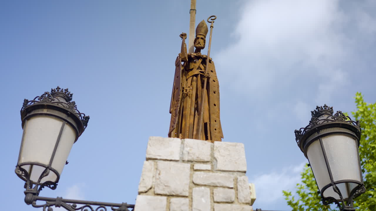 Rusty Statue of a Bishop atop a Stone Column with Lampposts