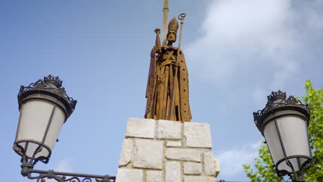 rusty statue of a bishop atop a stone column with lampposts