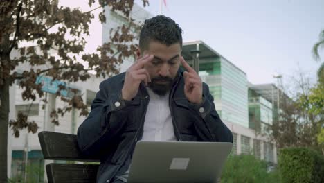 hombre barbudo serio trabajando con una computadora portátil al aire libre