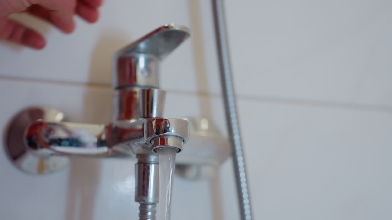 Close up of hand turning on bathroom water tap, stream of clear water flowing smoothly from shiny faucet, highlighting daily household routine