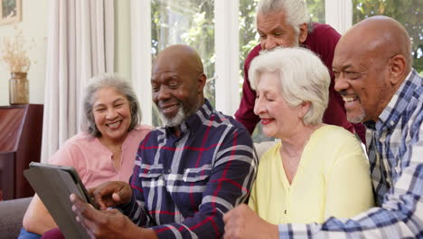 Happy-diverse-senior-male-and-female-friends-using-tablet-together-in-sunny-living-room,-slow-motion