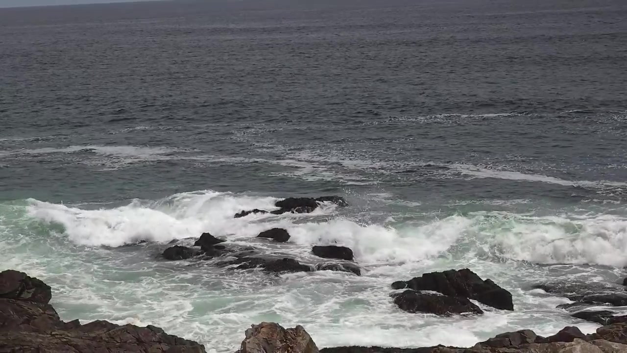 Rocce illuminate dal sole incontrano il mare mosso sotto un cielo blu con nuvole sottili. Nessuna persona, nessun animale. Costa calma, onde forti, terreno accidentato. Perfetto per progetti di viaggio, natura o avventura.