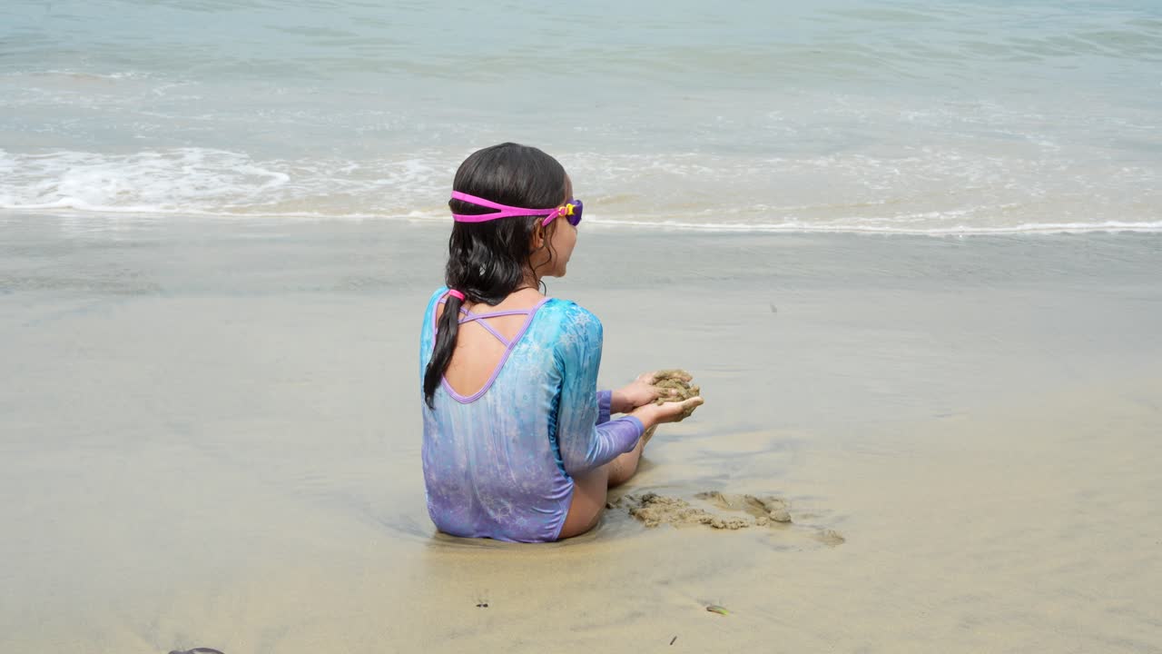 해변에 앉아 모래로 혼자 놀고 있는 아이의 뒷면