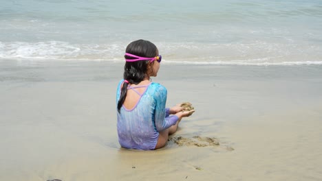 Back-view-of-a-kid-sitting-at-the-beach,-playing-alone-with-sand