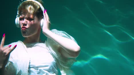 amazing under water shot of happy short haired young woman dancing, enjoying hard rock music in headphones slow motion.