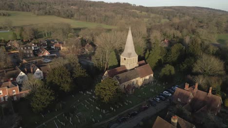 Aerial-orbits-St-James-Church-in-golden-light,-Shere,-Guildford,-UK