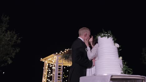 newlyweds making a kiss after cut of wedding cake, bride groom behind of wedding three-tiered cake