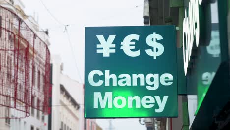 a green sign from a currency exchange business displays the words 'change money' alongside symbols representing various available currencies such as japanese yen, us dollar, and euro