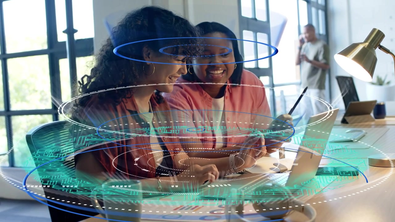 Two women working in business review, left typing causing AR charts on laptop, right showing phone