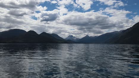 sobrevuelo aéreo idílico lago hacia la silueta de una cordillera gigante en el fondo durante un día nublado en la patagonia, argentina