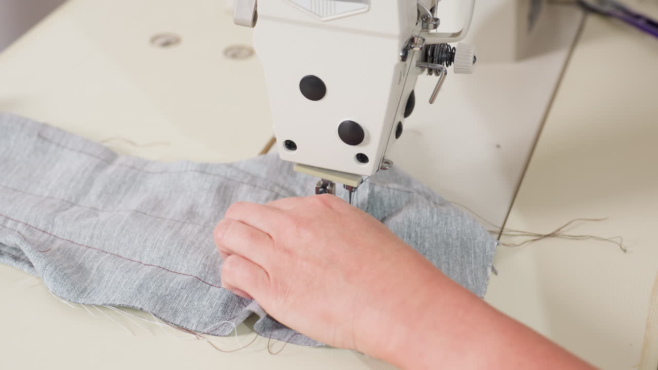 Hand view of tailor removing material from needle, cutting thread, ensuring seamless finish, showing precise garment craftsmanship, focusing on technique, neat edges, quality results