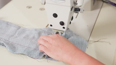 hand view of tailor removing material from needle, cutting thread, ensuring seamless finish, showing precise garment craftsmanship, focusing on technique, neat edges, quality results