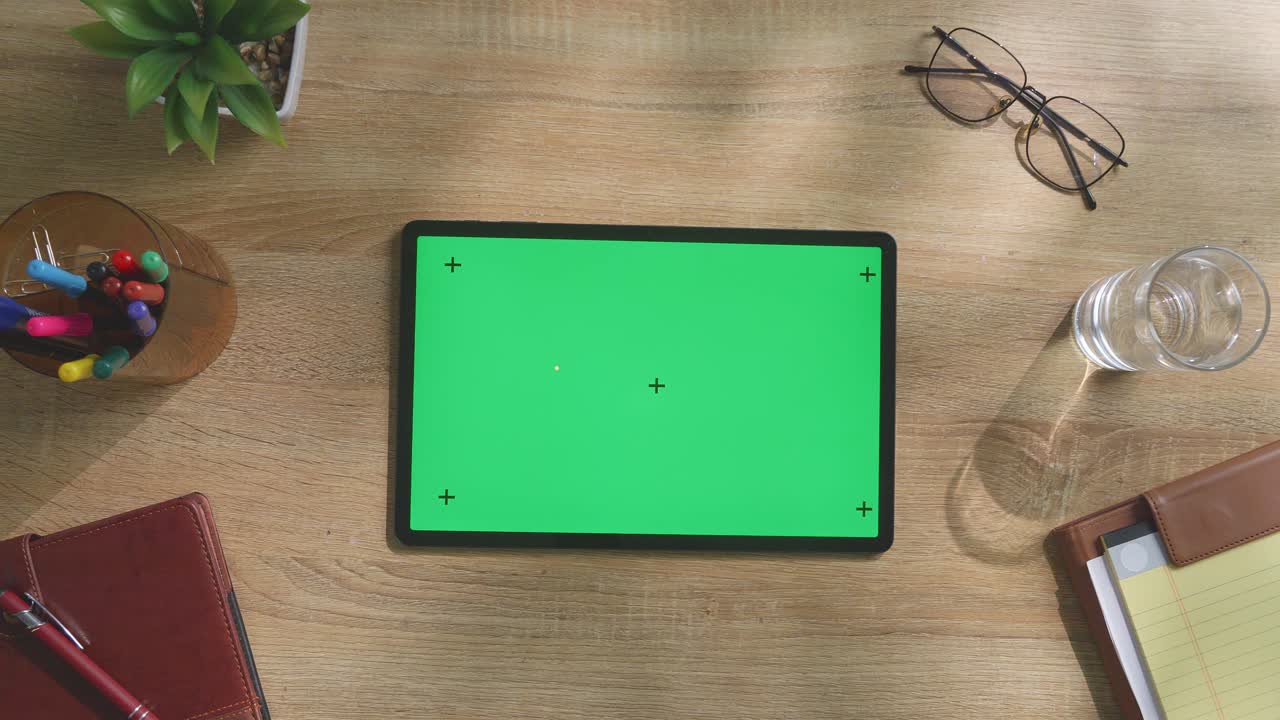 vista de arriba hacia abajo de una computadora portátil con pantalla verde simulada pantalla chromakey en un escritorio de oficina de madera al lado de la libreta con bolígrafos, gafas y un vaso de agua.