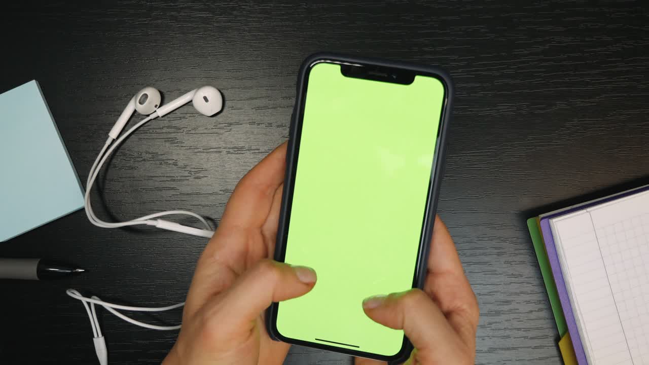 테이블 위에 초록색 화면이 있는 드폰: 여성 손가락이 초록색 스크린이 있는 휴대전화에 메시지를 입력하고 있다.