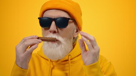 satisfied man enjoying smell of cigar indoors. old guy holding cigar in studio.