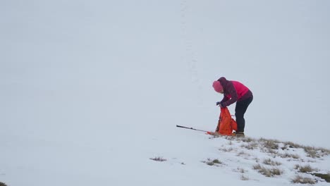 Frau-In-Rosa-Mantel-Und-Hut-überprüft-Ausrüstung,-Während-Sie-Im-Schnee-Steht