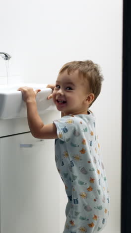 lovely toddler trying to reach water flowing from tap. baby boy jumping happily in the bathroom. vertical video