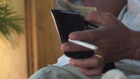 close up shot of an elderly asian man enjoying a cigarette whike placing dollar bills in his wallet