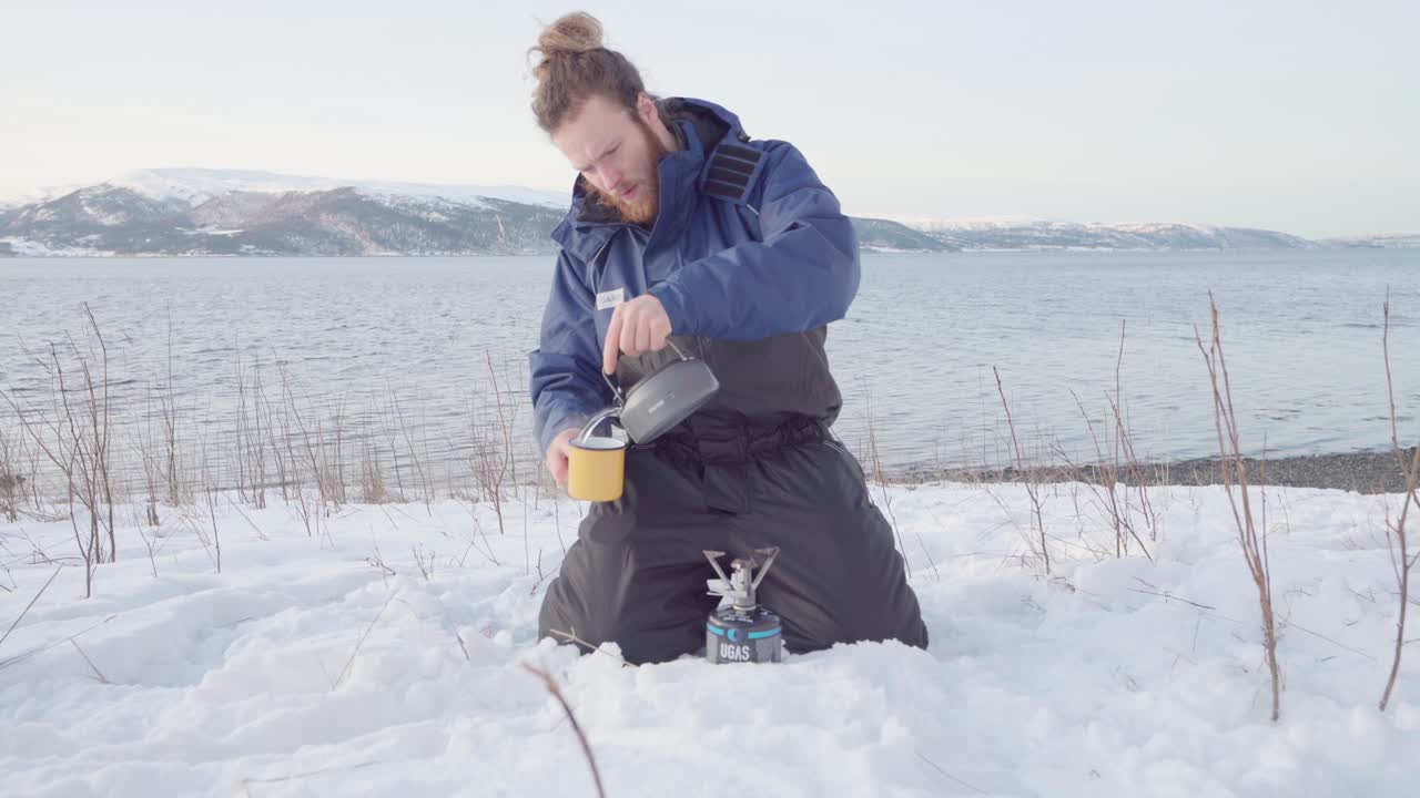 바다 경치를 배경으로 컵에 뜨거운 드링크를 붓는 야영자