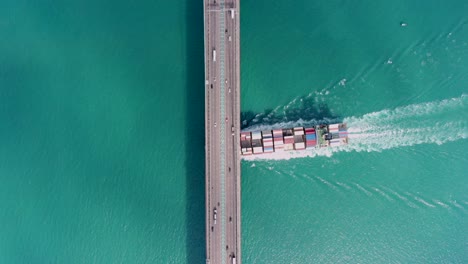 large container ship passing under a bridge with traffic in hong kong bay, aerial view