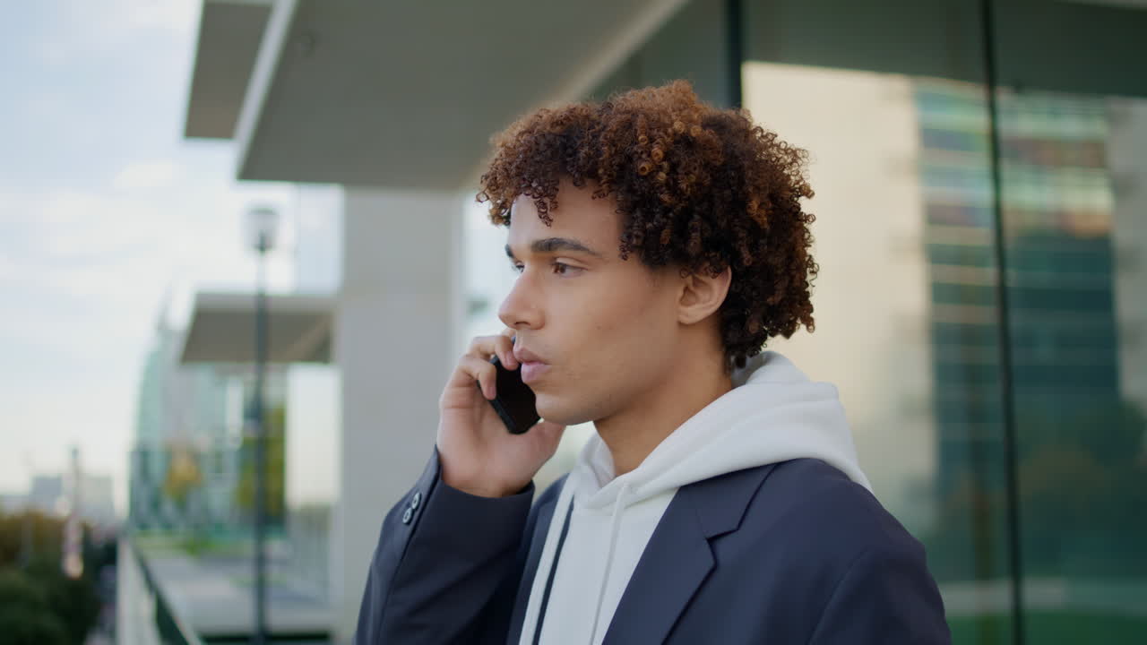 Young man having mobile call at glass balcony close up. Curly guy using phone