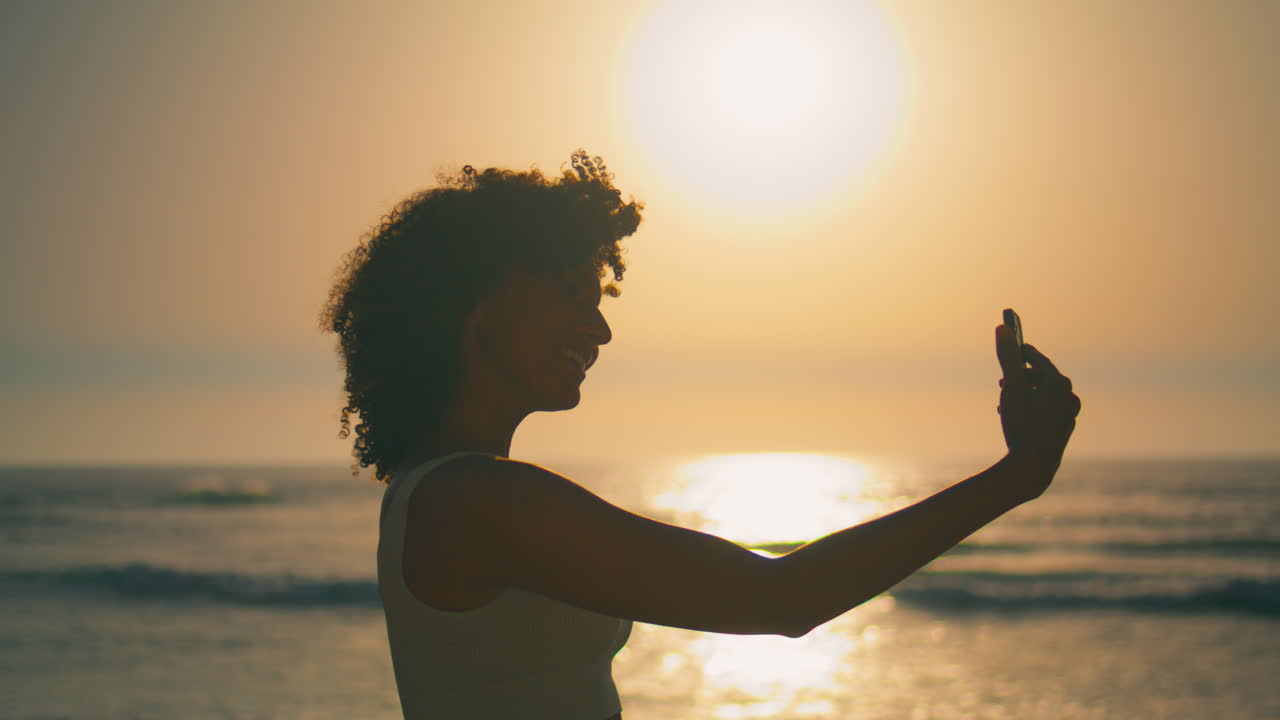 ragazza sorridente telecamera del telefono in piedi sulla spiaggia all'alba close-up. donna che fa selfie
