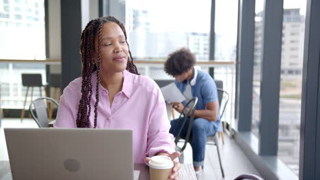 smiling woman holding coffee cup and using laptop in modern office setting