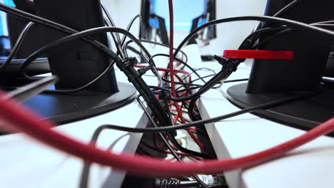 messy cables and wires creating a chaotic scene under computer monitors in an office workplace