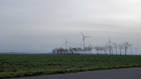 Panning-shot-of-a-windmill-farm,-in-a-country-cultivated-field,-on-a-cloudy-and-windy-evening