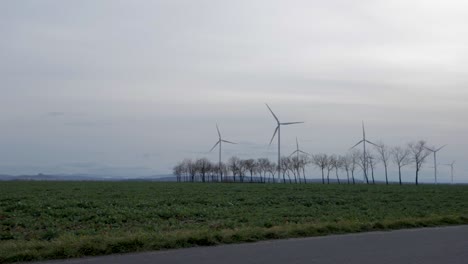 panning shot of a windmill farm, in a country cultivated field, on a cloudy and windy evening