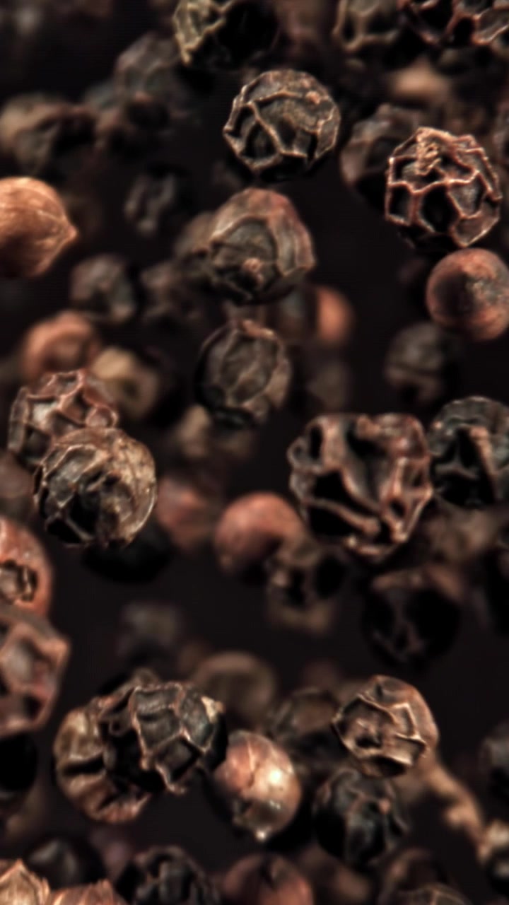 Vista macro di grani di pepe nero che cadono e vanno a fuoco.
