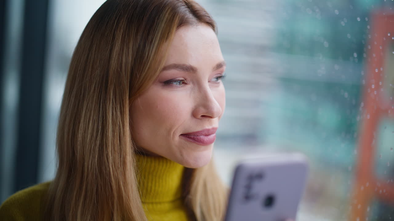 Cheerful lady reading smartphone chat standing by window closeup. Smiling woman