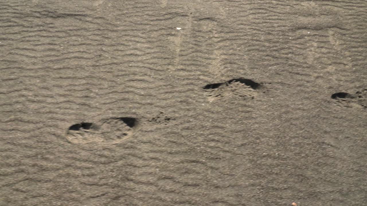 Tomada panorâmica aproximada de pegadas em uma praia de areia branca em Sandur, na Ilha de Sandoy, durante um dia ensolarado