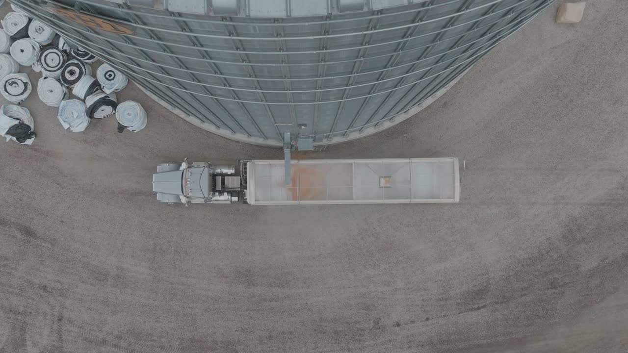 Drone footage of trucks semi loading corn at farmstead grain bin.