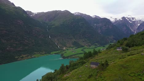 Yrisetra-Pequeñas-Cabañas-En-Lo-Alto-De-La-Antigua-Ladera-De-La-Montaña-Con-El-Glaciar-Briksdal-En-El-Fondo-De-La-Montaña---Impresionante-Vista-Aérea-Desde-El-Increíble-Mirador-De-La-Ladera-En-Un-Destino-Popular-En-Nordfjord