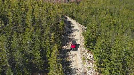 off-road-vehicle-Jeep-truck-driving-crawling-down-rocky-dirt-logging-road-on-mountain-surrounded-by-green-trees-and-forest-wide-Aerial-reversing-tracking-SUV-as-it-descends-slowly-carefully-skillfully